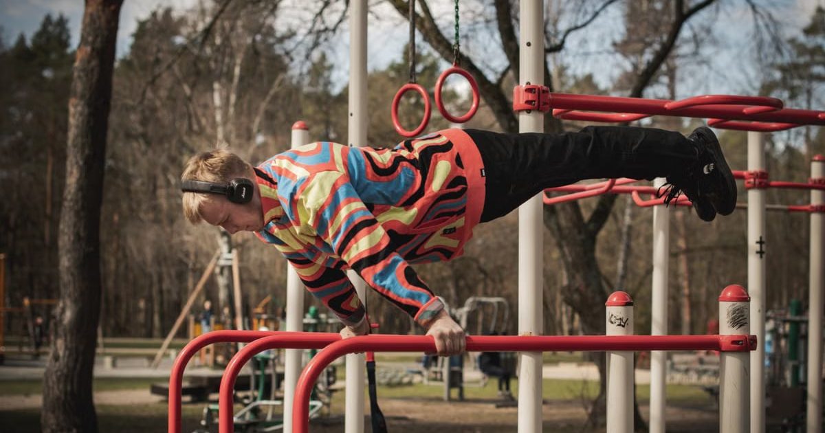 Young adult man exercises on outdoor gym bars in a colorful outfit in Vilnius, Lithuania.
