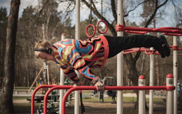 Young adult man exercises on outdoor gym bars in a colorful outfit in Vilnius, Lithuania.